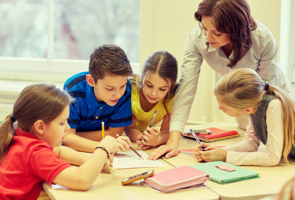 A teacher works with students to help them answer a question, which they're solving on a sheet of paper.