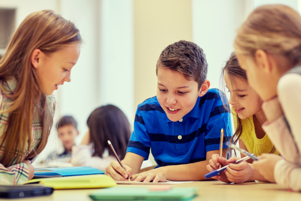 A group of four elementary students sits at a desk, working to solve a question using pencils and paper.