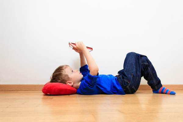 A student lays on the floor, looking up at his tablet.