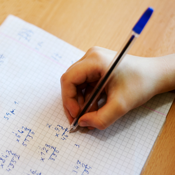 een student vult vermenigvuldigingsvragen in met een blauwe pen en een vel grafisch papier.