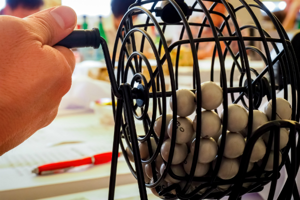 A hand rotates a basket filled with bingo balls.